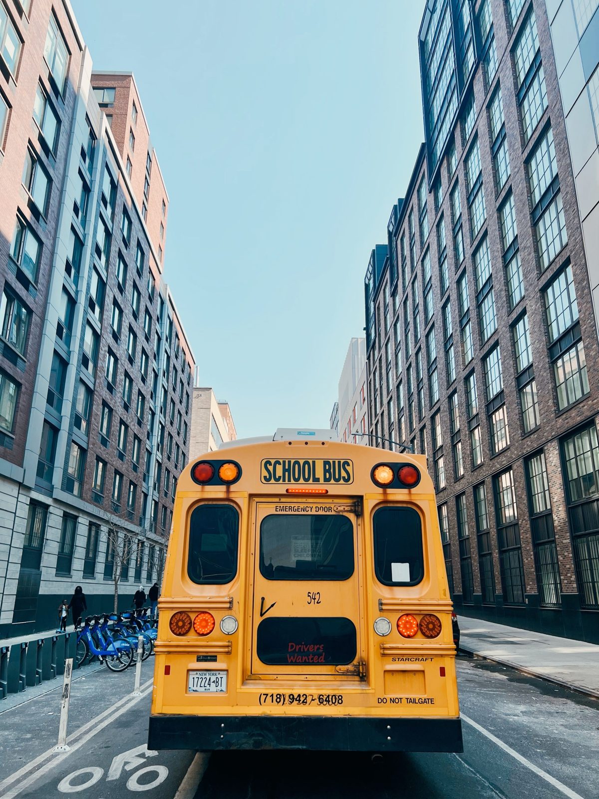 A yellow school bus on a narrow street between NYC buildings